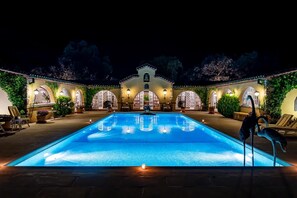 A swimming pool with a fountain, surrounded by arched windows and outdoor seating.