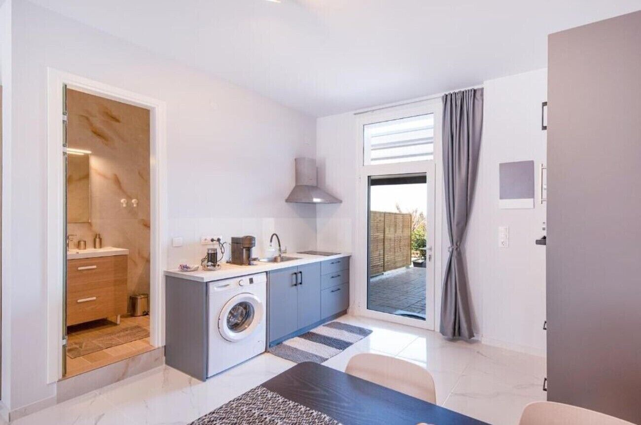 A modern kitchen with a washing machine, a sink, and a window with curtains.