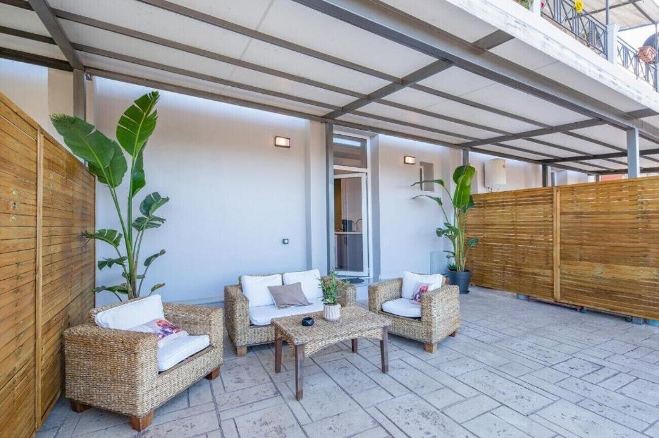 A covered outdoor seating area with wicker furniture and potted plants.