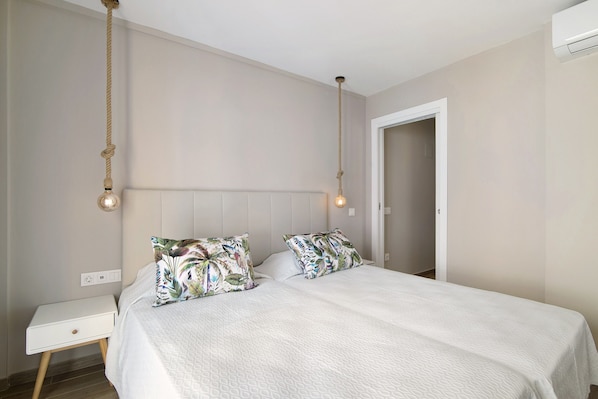 A bedroom with a bed, bedside tables, a hanging light fixture, and a door.