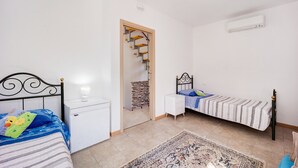 Une chambre avec deux lits, une table de chevet blanche, une commode, un tapis à motifs et un escalier menant à une autre pièce.