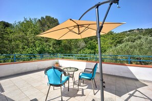 Une terrasse avec deux chaises, une table et un grand parasol.