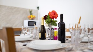 Une table à manger dressée avec des assiettes, des verres et des bouteilles, dont une bouteille de champagne et un vase contenant une rose rouge.