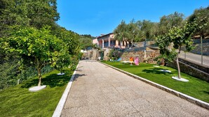 Un chemin pavé mène à un bâtiment à la façade en pierre, entouré de pelouses et d’arbres bien entretenus.