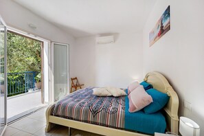 Une chambre avec un lit, une table de chevet, un climatiseur fixé au mur et un balcon donnant sur un paysage verdoyant.