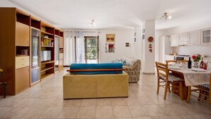 Un salon avec un canapé, une table à manger avec des chaises, un coin cuisine et une grande fenêtre avec des rideaux.