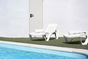 A swimming pool with two white lounge chairs and a door.