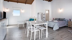 A modern room with a dining table, chairs, a sofa, a bed, a TV, and a window. - Holiday Home 'La Teja 3' with Private Pool, Wi-Fi and Air Conditioning (Vejer de la Frontera)