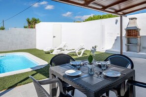 Une terrasse avec une table à manger pour quatre personnes, une piscine et un barbecue.