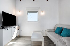 Un salon moderne doté d’un téléviseur à écran plat, d’une table blanche, d’un canapé avec des coussins turquoise et d’une fenêtre offrant une vue agréable.