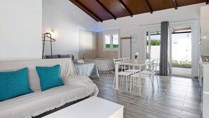 A modern living room with a sofa, a dining table with chairs, a kitchen area, and a view through a glass door. - Holiday Home 'La Teja 3' with Private Pool, Wi-Fi and Air Conditioning (Vejer de la Frontera)