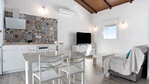 A modern kitchen with a patterned backsplash, a dining area with white furniture, a flat-screen TV, and a cozy seating area with a blanket. - Holiday Home 'La Teja 3' with Private Pool, Wi-Fi and Air Conditioning (Vejer de la Frontera)