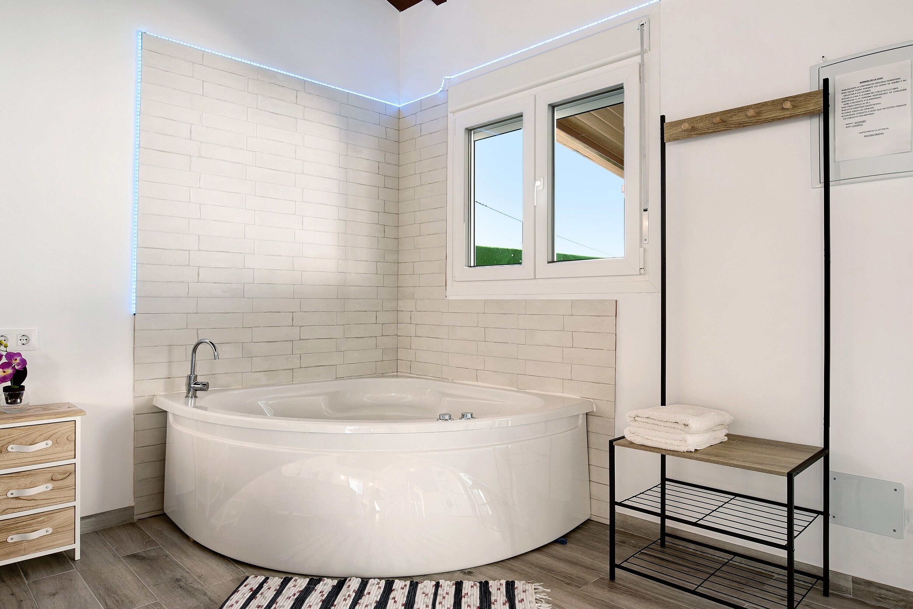 Un bagno moderno con una vasca freestanding, un mobile lavabo in legno, un piccolo ripiano con asciugamani e una finestra vista verde.
