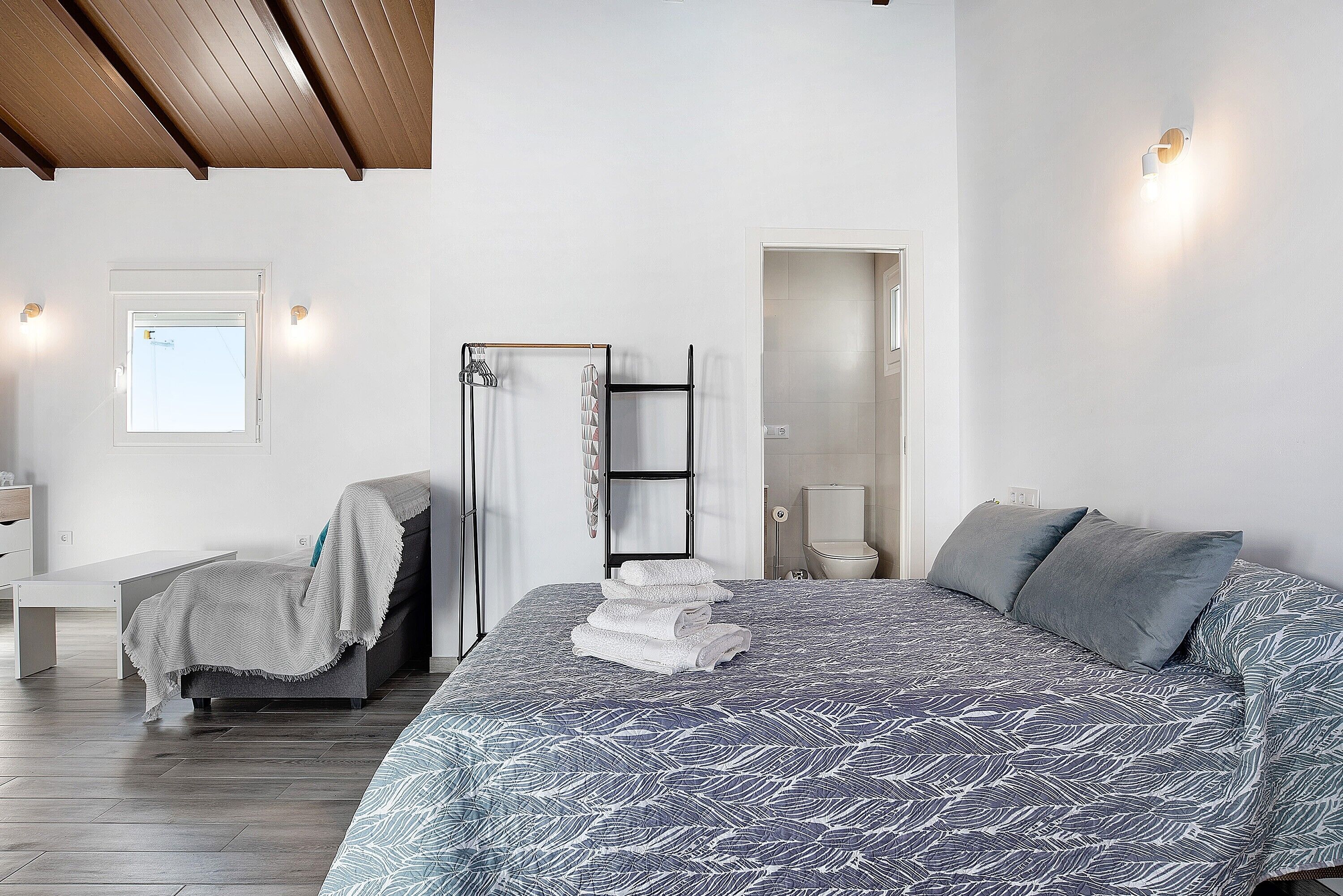 Une chambre moderne avec un grand lit, un banc, une échelle et une porte de salle de bain.