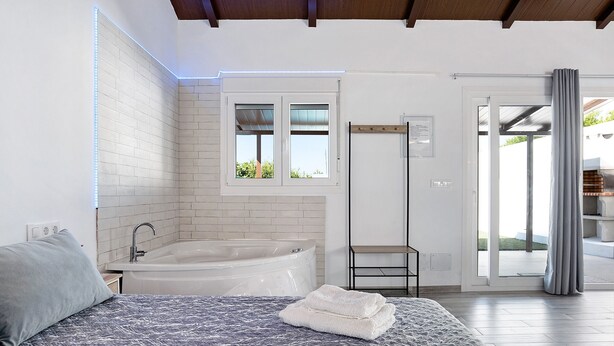 A bedroom with a bed, a window, a bathtub, and a shower area. - Holiday Home 'La Teja 3' with Private Pool, Wi-Fi and Air Conditioning (Vejer de la Frontera)