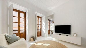 A living room with a sofa, a TV, a white console, and a large window.