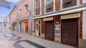 A street with buildings, one with a closed shutter and a sign reading 'MOGADOR.'