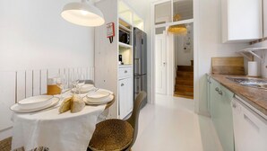 A modern kitchen with white cabinetry, a dining table set for four, and a visible staircase leading to another level.