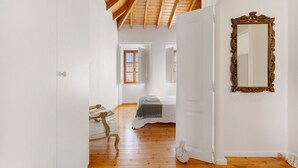 A hallway with a wooden ceiling, a bed with a white bedspread, and a large ornate mirror on the wall.