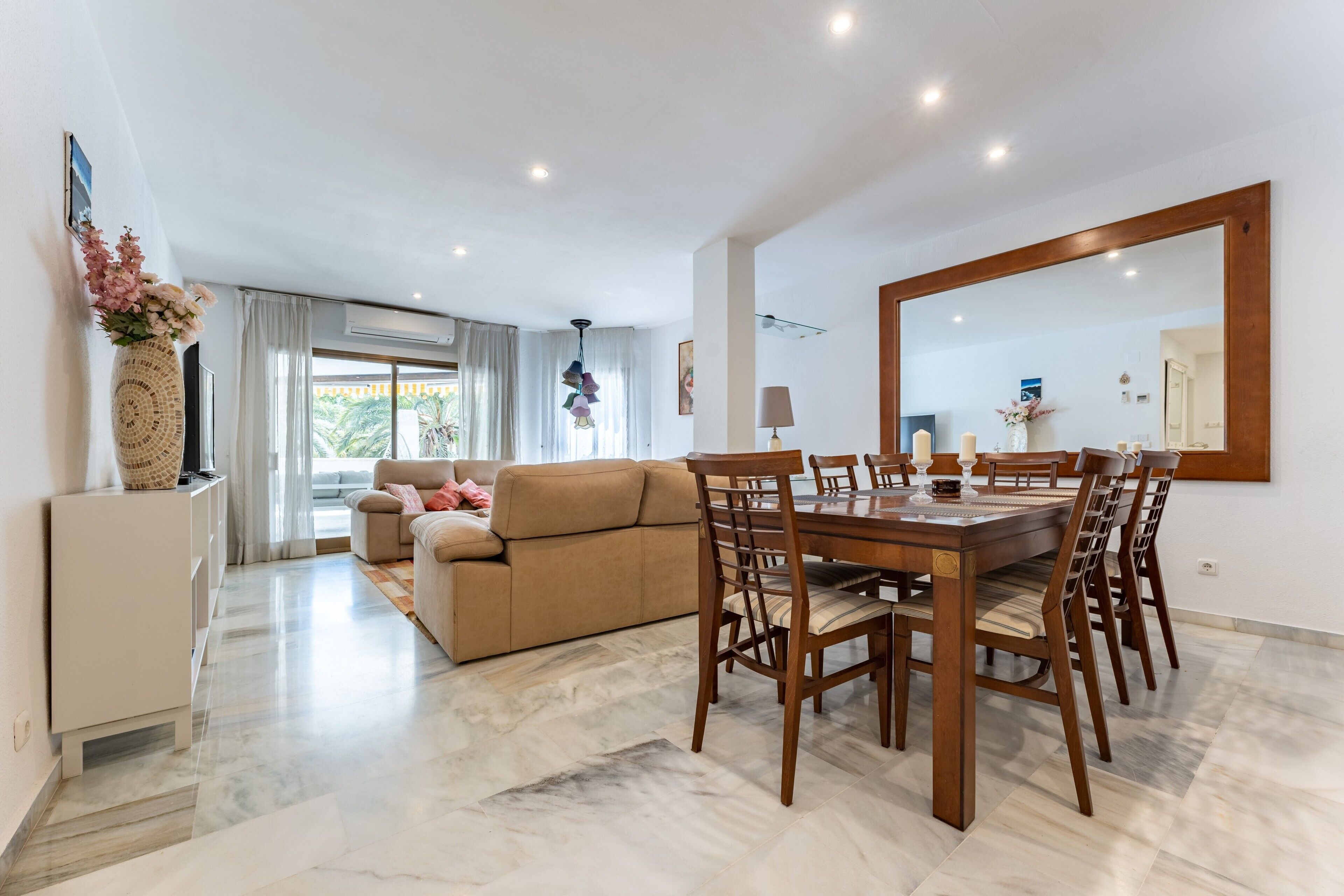 A spacious living area with a dining table, sofa, and a large mirror.