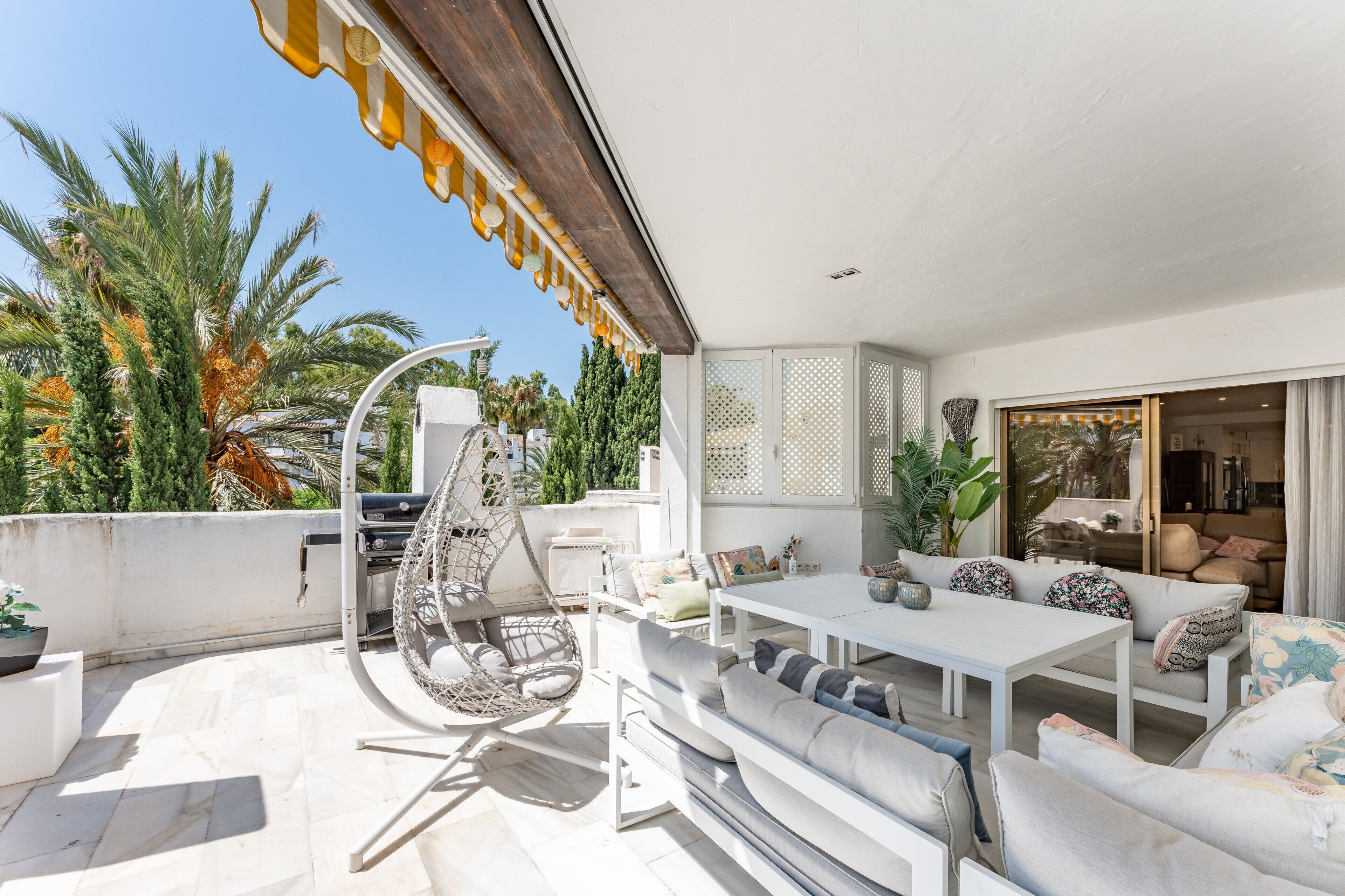 Une terrasse sur le toit avec une table blanche, des sièges confortables, un fauteuil suspendu et un barbecue.