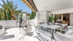 Une terrasse sur le toit avec une table blanche, des sièges confortables, un fauteuil suspendu et un barbecue.