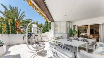 Une terrasse sur le toit avec une table blanche, des sièges confortables, un fauteuil suspendu et un barbecue.