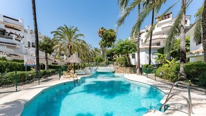 Une piscine à l’eau d’un bleu cristallin, entourée de palmiers et bordée d’un bâtiment blanc doté de balcons.