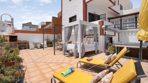 Une terrasse sur le toit avec des chaises longues, un espace salon couvert et des plantes en pot.