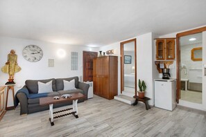 Una sala de estar con un sofá, una mesita de centro, un armario de madera y un refrigerador pequeño.