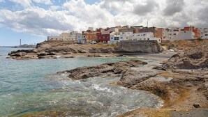 Une ville côtière avec des bâtiments situés sur un littoral rocheux, une eau claire et un ciel partiellement nuageux.