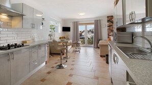 Une cuisine moderne avec un coin repas, un téléviseur et une vue sur l’extérieur grâce à la porte vitrée.