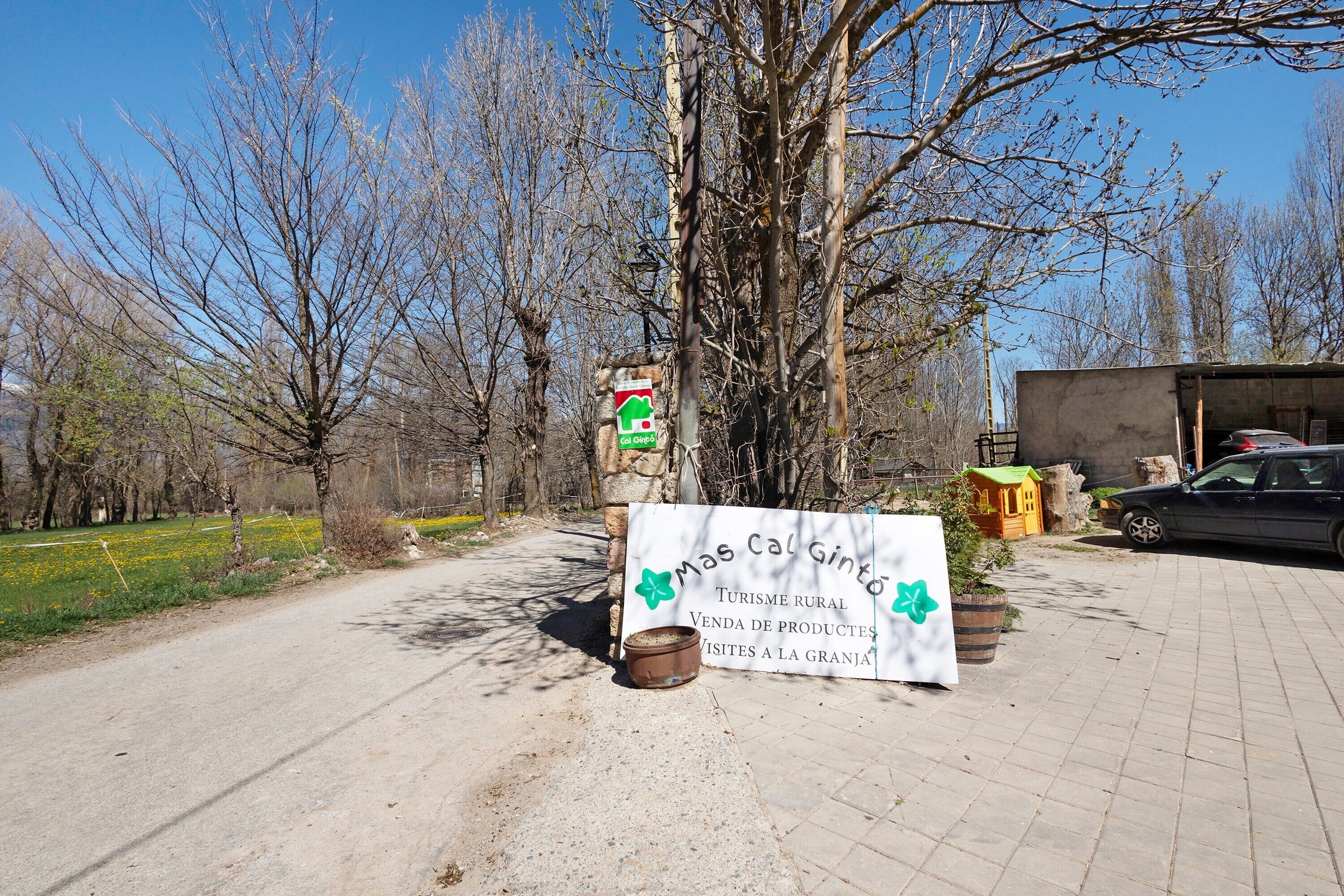Un panneau indiquant un site touristique rural, avec en arrière-plan un décor rustique, un mur de pierres et une voiture garée.