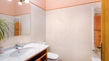 Un baño con lavamanos, espejo, toallero y retrete.