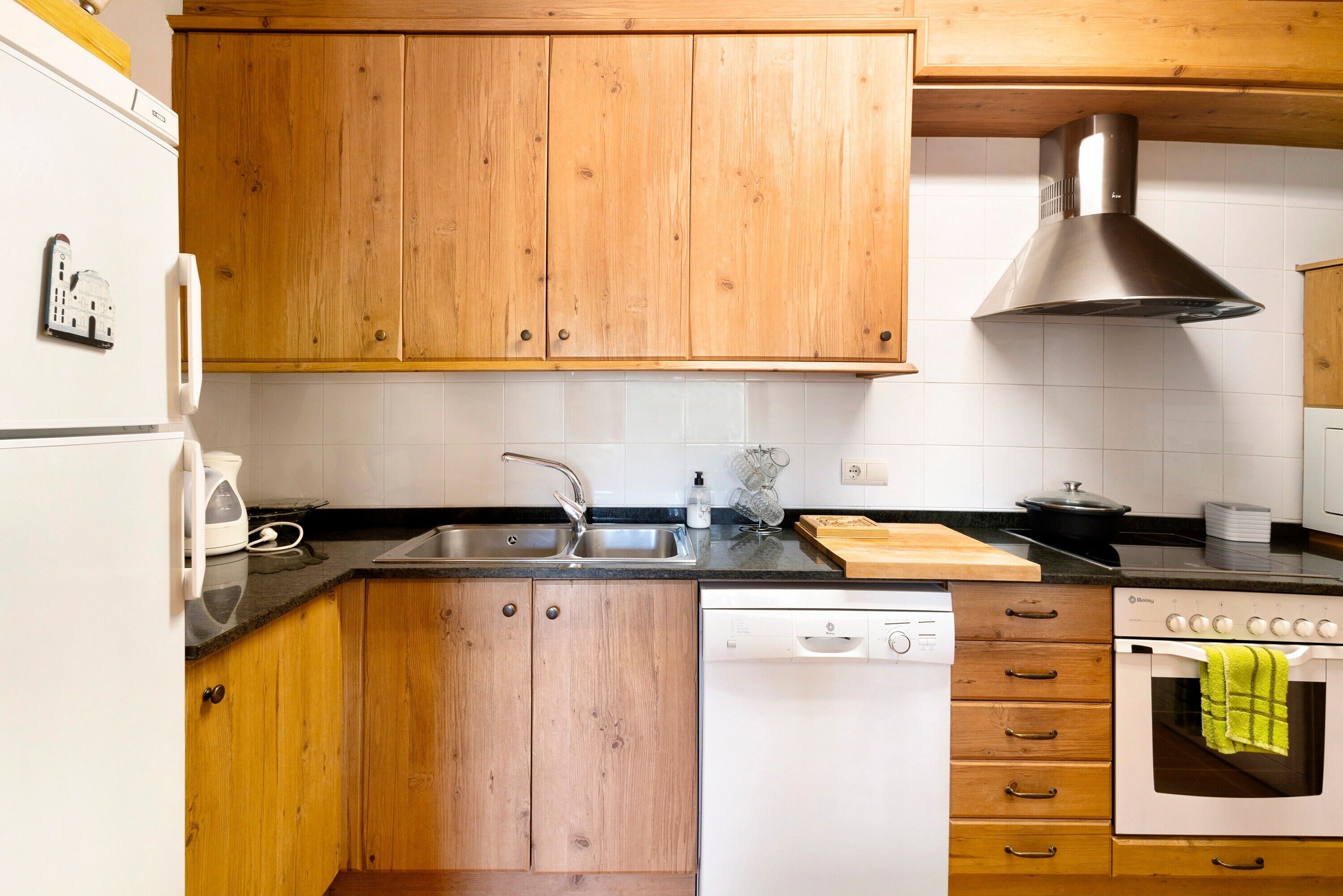 Una cocina con armarios de madera, un lavamanos de acero inoxidable, un lavavajillas, un horno y una campana extractora.