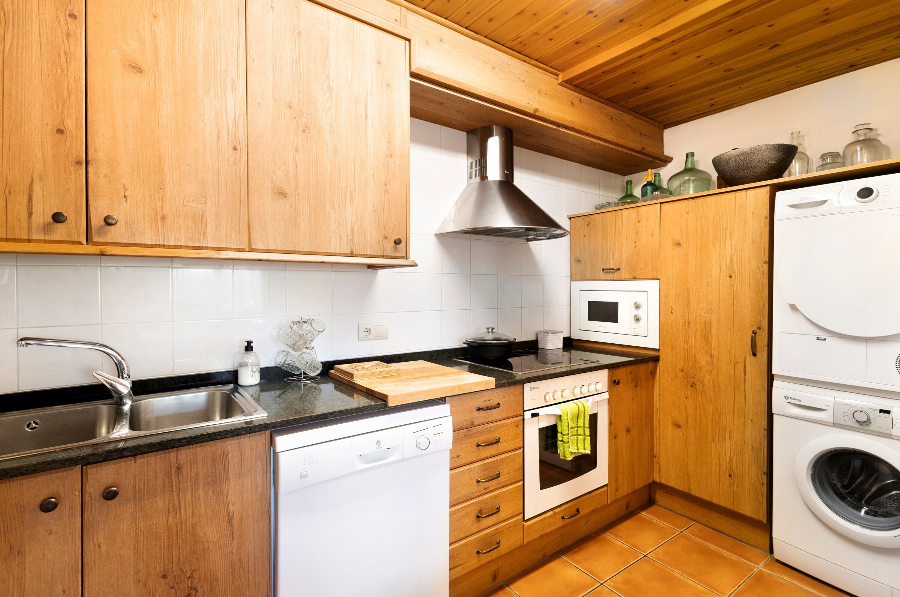 Une cuisine dotée de meubles en bois, d’un évier en acier inoxydable, d’un lave-vaisselle, d’un four et d’un lave-linge.