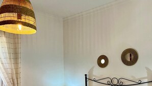 A bedroom with a bed, a hanging lamp, a nightstand with a lamp, and two wall mirrors.
