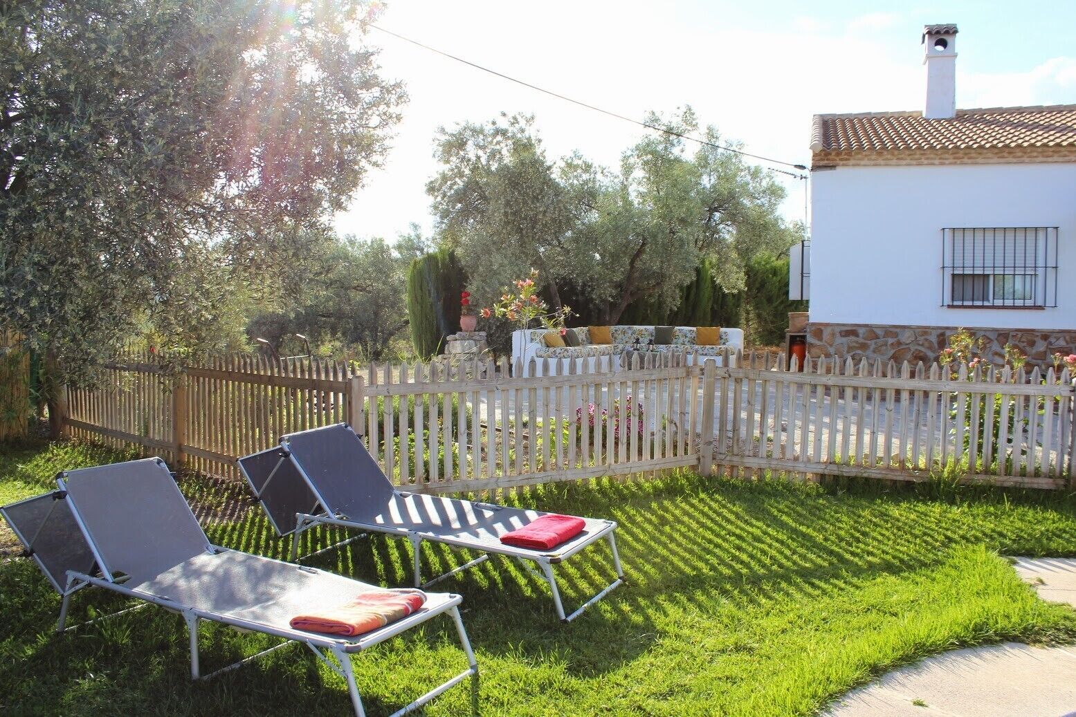 A fenced backyard with two lounge chairs, a white house, and a garden.