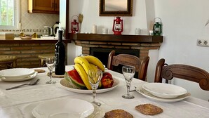 A dining table set with plates, cutlery, and fruit, a fireplace, and a kitchen area with cabinets and a window.