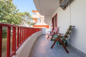 Ein Balkon mit roter Geländer, zwei Klappstühlen und einem gefliesten Boden.