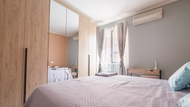 A bedroom with a bed, a wooden wardrobe, a desk with a lamp, and a window with curtains. - Vacation Home "La Casa Di Wioletta" with Sea View, Private Terrace & Wi-Fi (Barcellona pg)