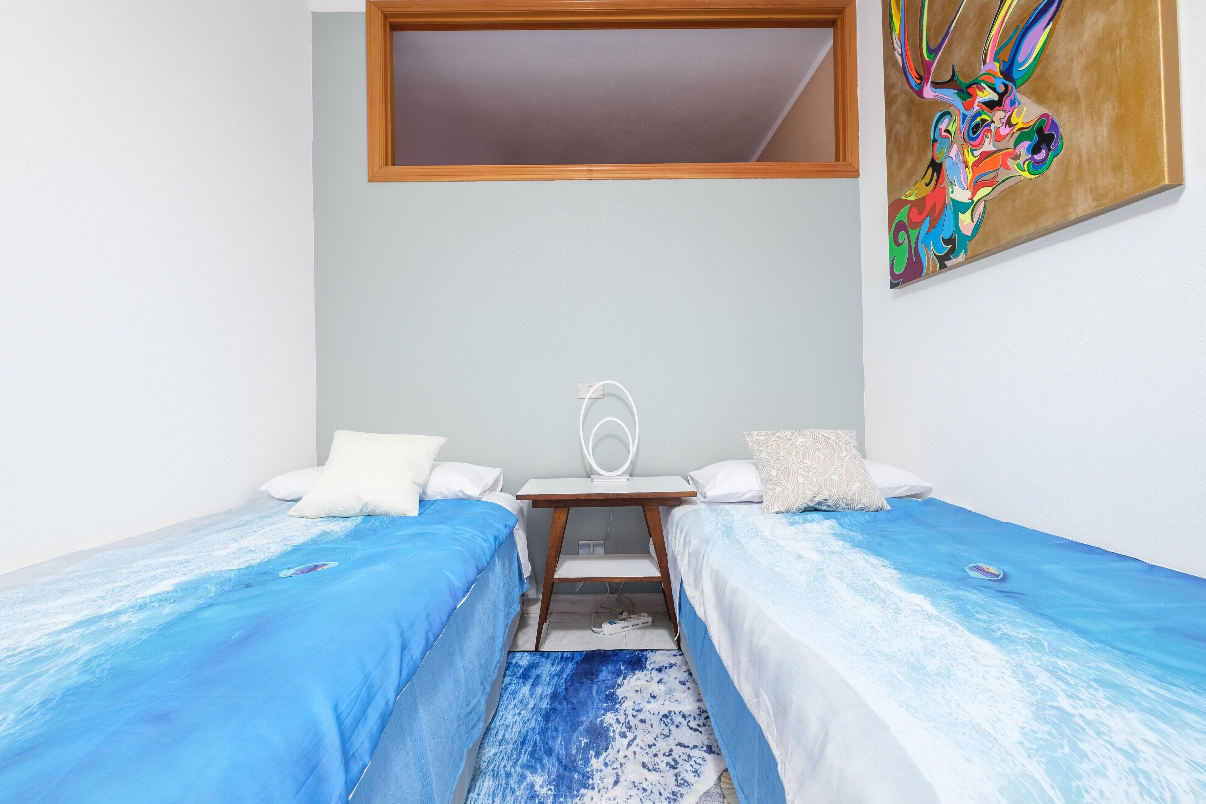 Une chambre avec deux lits, un bureau, une chaise, une fenêtre et un tableau au mur.