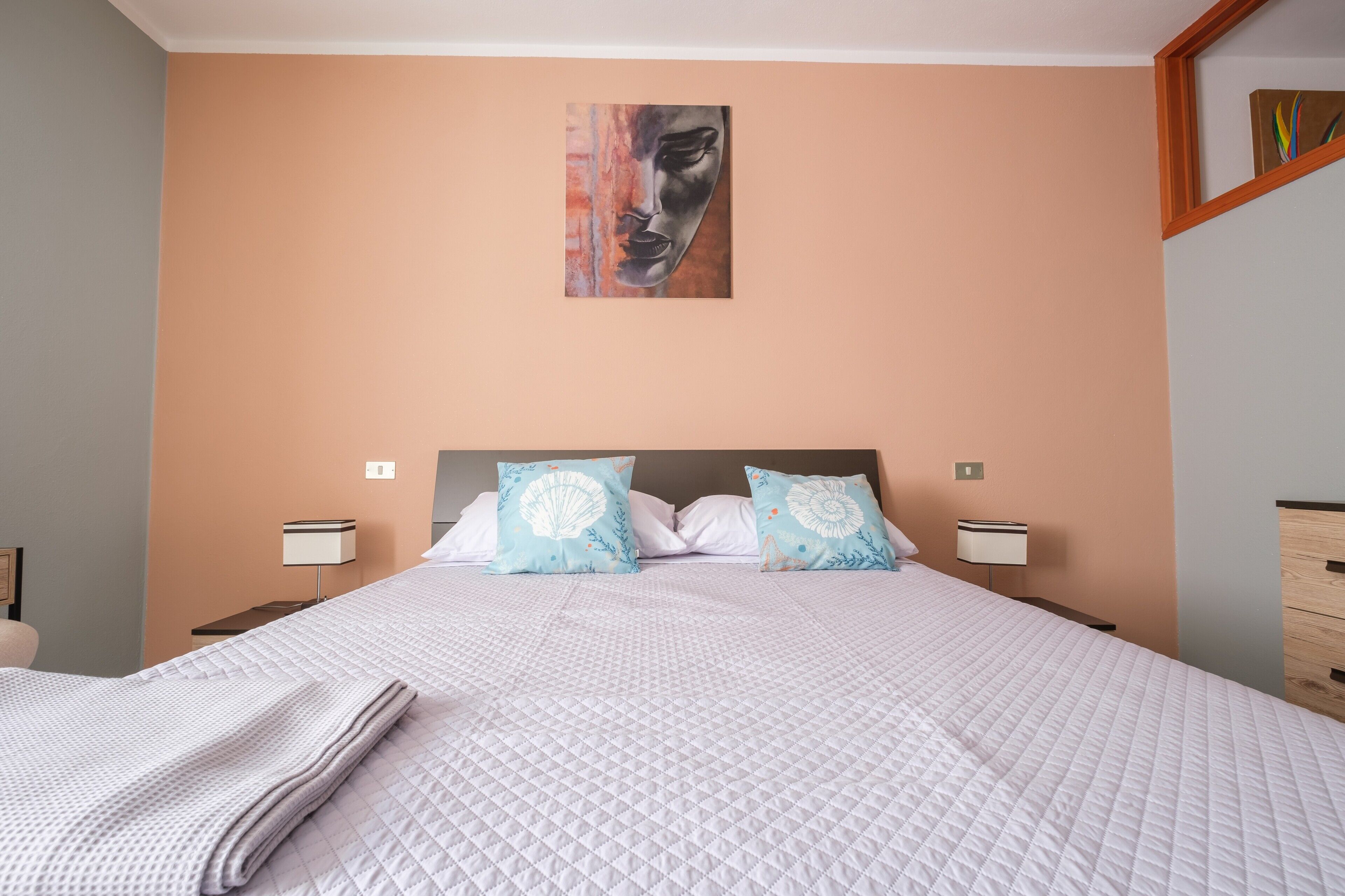 A neatly made bed with a quilted pattern, two decorative pillows, a wall-mounted artwork, and bedside lamps.