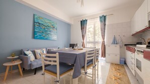 A dining area with a table set for four, a sofa, a small side table, and a kitchen area with cabinets and a stove. - Vacation Home "La Casa Di Wioletta" with Sea View, Private Terrace & Wi-Fi (Barcellona pg)