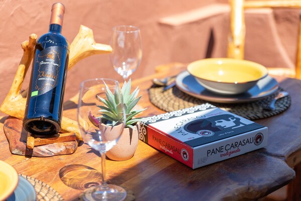 A bottle of wine, a glass, a box of Pane Carasau, and a small plant on a wooden table. - Holiday Home 'Hakéyah' with Sea View, Wi-Fi and Air Conditioning (Castelsardo)