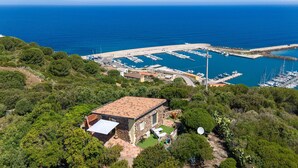 A coastal property with a stone building, a marina with boats, and a clear view of the sea.