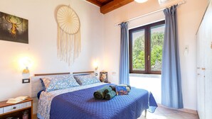 A bedroom with a bed, a bedside table with books, a dreamcatcher, and a window with curtains.