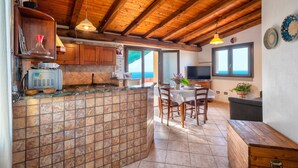 A kitchen with a tiled backsplash, wooden ceiling beams, a dining area with a table and chairs, and a television.