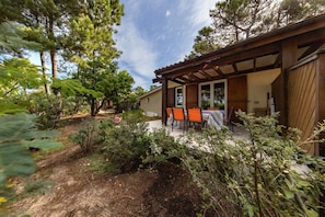Une terrasse couverte avec des sièges d’extérieur, entourée d’arbres et d’un jardin.