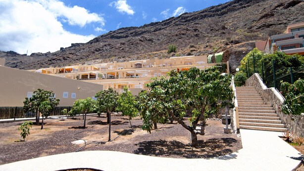 A courtyard with a staircase leading to a building, surrounded by trees and a mountainous backdrop.